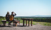 Two women sitting on a bench looking out over the landscape with Kinnekulle at the horizon. 