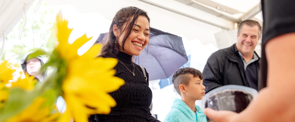 En ung kvinna ser glad ut och pratar med några andra personer i ett tält.