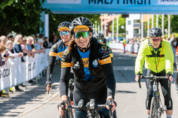 Tjej på cykel, glad och två personer till bakom