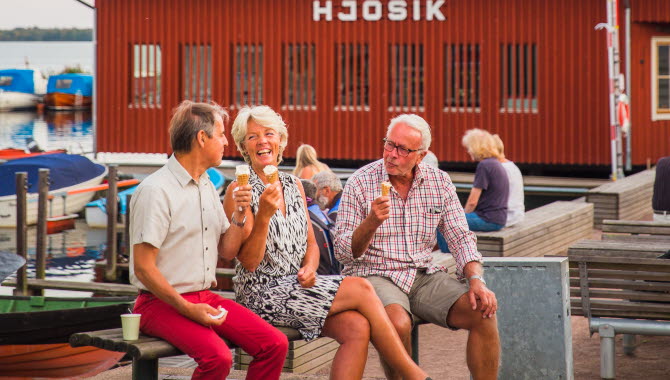 Tre människor äter glass i Hjo hamn, med fiskaffären Hjo Sik i bakgrunden.