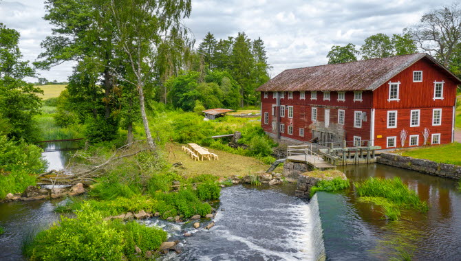 En stor röd gammal kvarn vid brusande vatten och gröna omgivningar.