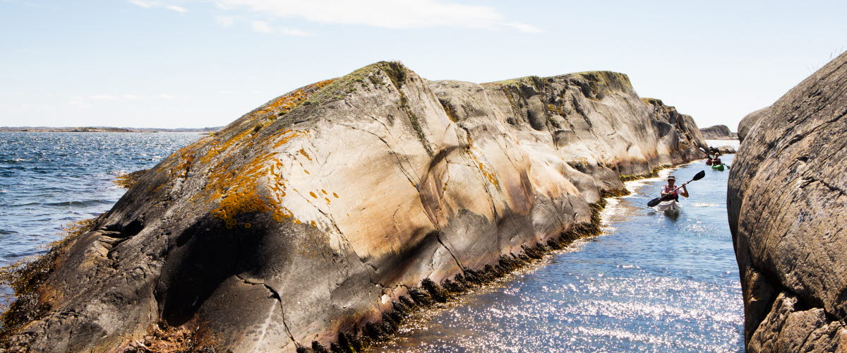 En person i kajak paddlar igenom en smal kanal mellan två klippor i Kosterhavet utanför Kosteröarna.