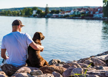 Ung man med hund som sitter i Hjo hamn och tittar ut över Vättern och Hjo stad. 