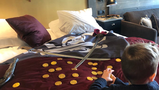 Ett barn leker med guldmynt och sjörövarsvärd på en dubbelsäng på Daftö Pirathotell.