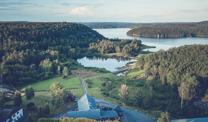 En bild tagen ovanifrån på en hotellverksamhet som ligger inbäddat i grönska framför en sjö.