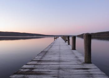 En bild på en frostig träbrygga som sträcker sig ut i en spegelblank sjö.