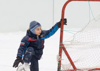 En pojke som sitter ute på is vid ett hockeymål