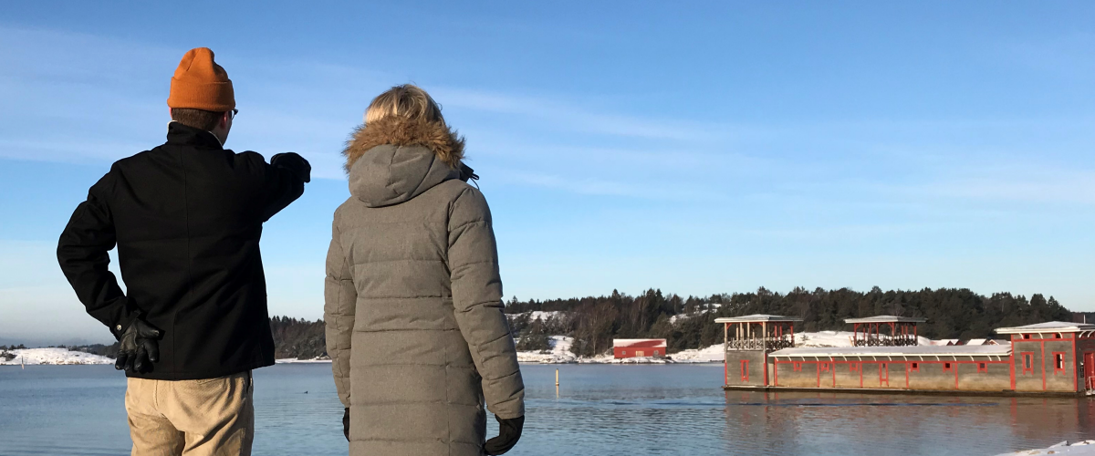 En man och en kvinna står och blickar ut över havet och Strömstads kallbadhus i vinterskrud.