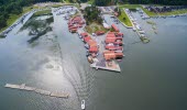 Aerial view over Spikens fishing harbour. Two lanes of red houses along the wharf surrounded by water. A boat is leaving the harbour creating waves behind.