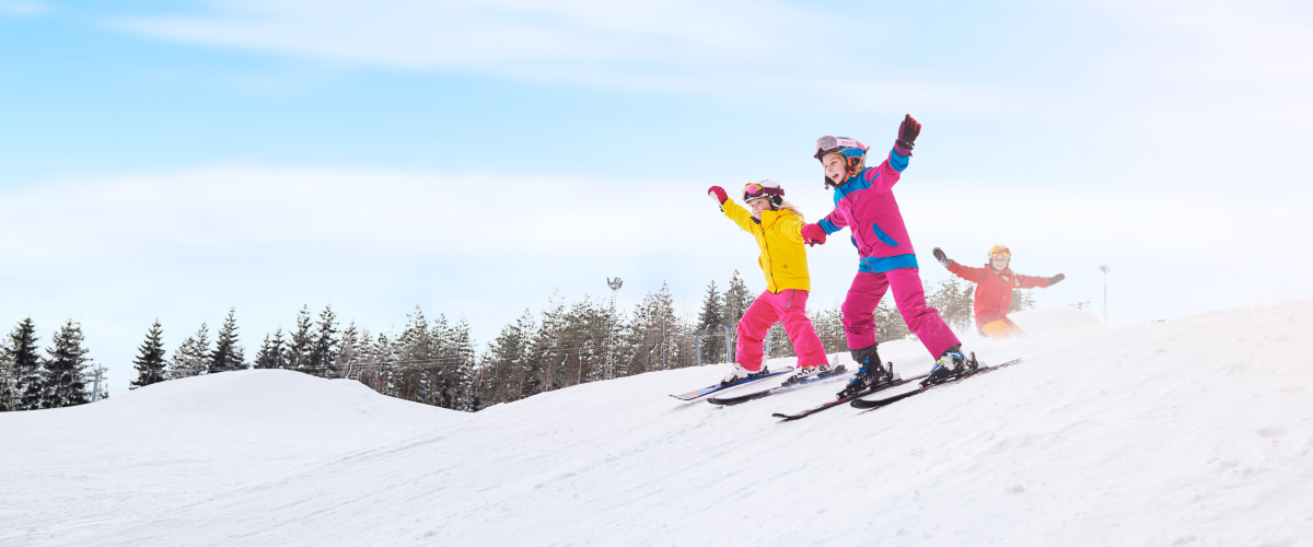 Två barn i färgglada kläder åker slalom på Ulricehamn Ski Center samtidigt som de håller varandra i handen. 