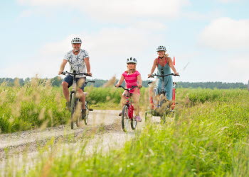 Två vuxna och ett barn cyklar på en grusväg. 