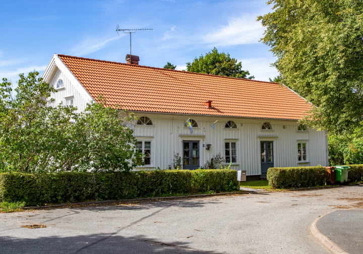 En bild på ett vackert vitmålat gammalt hus omgivet av gröna buskar.