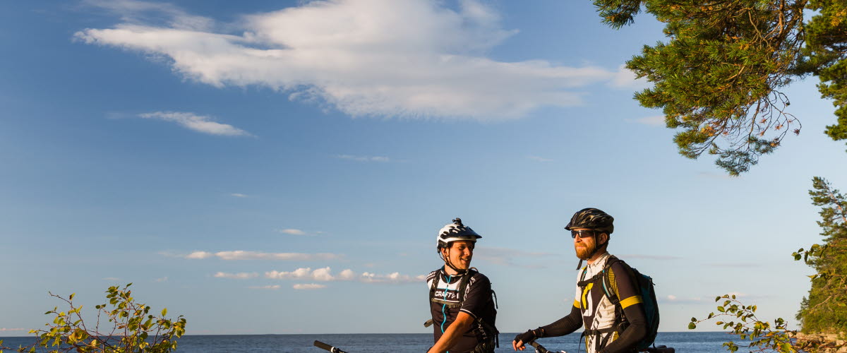 Two men take a break from their MTB cycling and look out over the water in the evening sun.