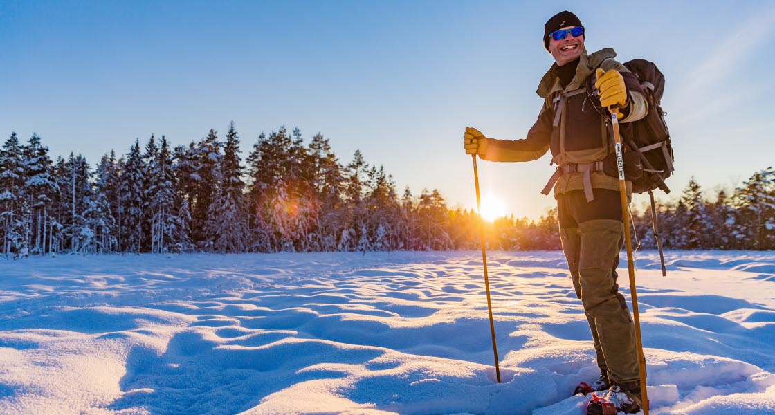 A beautiful sunny winter landscape. A person stands in the snow with skis on his feet and ski poles in their hands.