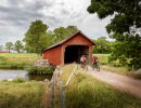 En man och en kvinna cyklar på en grusväg vid det unika långa brohuset, Vaholms brohus.