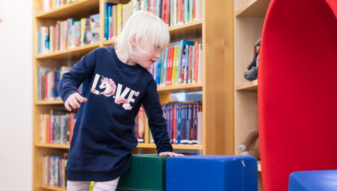 Ett barn försöker sätta sig till rätta bland sittpuffarna i biblioteket.