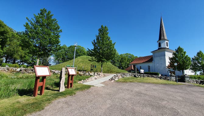 En översiktsbild över Flistad kyrka och Kung Ranes hög med informationsskyltar i förgrunden.
