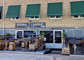 En bild på ett tegelhus med gröna markiser neddragna framför fönstren. Här finns också en entré till en pizzeria.