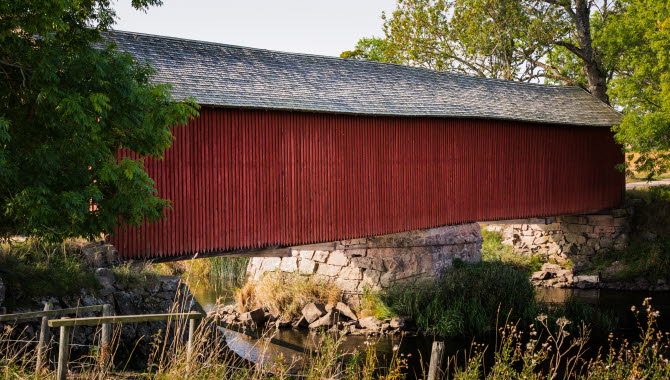 En röd övertäckt träbro går över ett stilla vattendrag