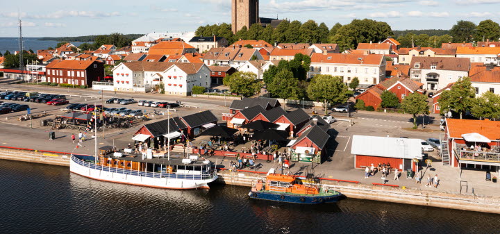 Flygfoto över bodarna i Mariestads gästhamn. Del av Gamla Stan med domkyrkan. Båtar i vattnet i förgrunden.