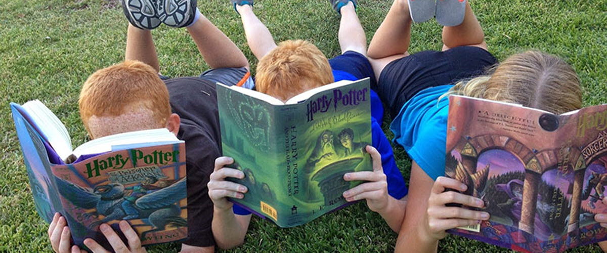 Barn som ligger på mage i gräset och läser en bok. 