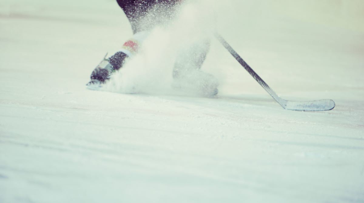 En bild på underkroppen av en person på is som bromsar med skridskorna så att det skvätter is