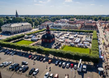Flygbild över Rådhuset och torget en solig dag. På torget är det marknad med flera stånd uppställda.