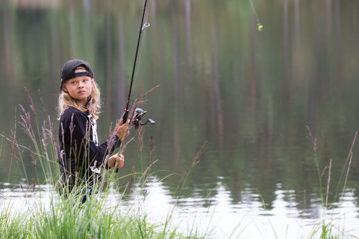 Ett barn står och fiskar vid en sjö.