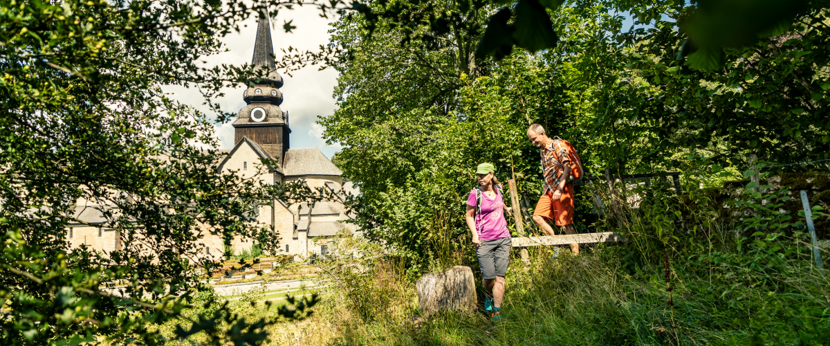 Man och kvinna som vandrar i gröngräset med Varnhems klosterkyrka i bakgrunden.