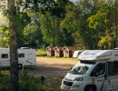 Campingplats med husbilar och röda stugor.