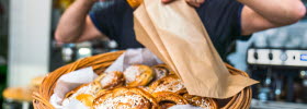 Café owner puts newly baked cinnamon buns in a bag. 