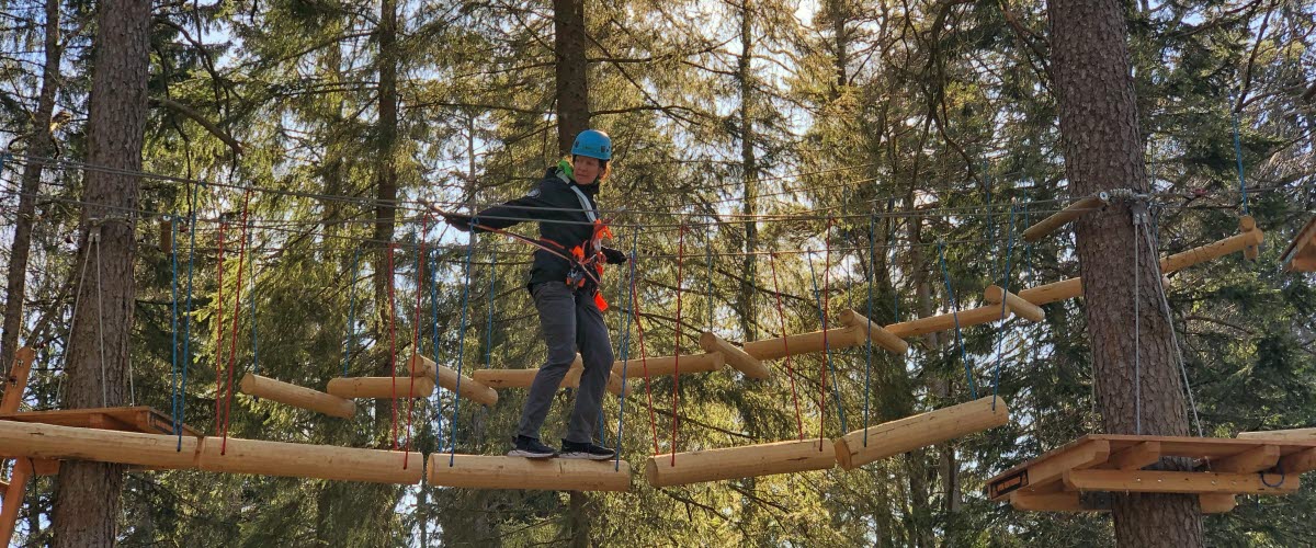 En person balanserar på hängande trästockar flera meter upp i luften i höghöjdsbanan på Billingen Skövde. 