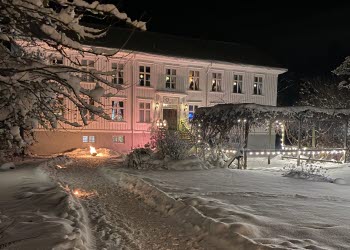 En vitt stort gammalt hus som är inbäddat i tjockt snötäcke.