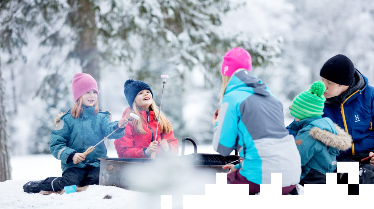 En familj sitter ute i snön och grillar korv