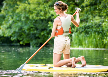 En kvinna sitter på knä på en SUP-bräda i vattnet.