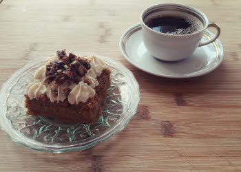 En bild på en kopp kaffe och en kaka på ett fat som står på ett bord.