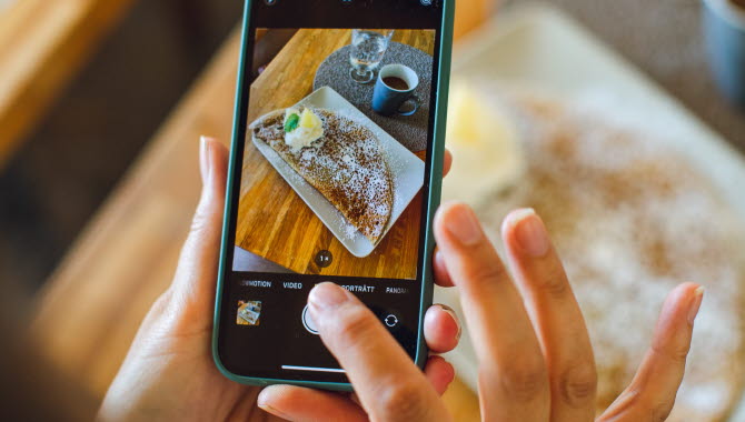 En person tar en bild med en smartphone. I telefonen syns bilden som är på en galette och en kopp kaffe.