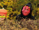 3 personer i halloweenmasker tittar upp bakom en buske.
