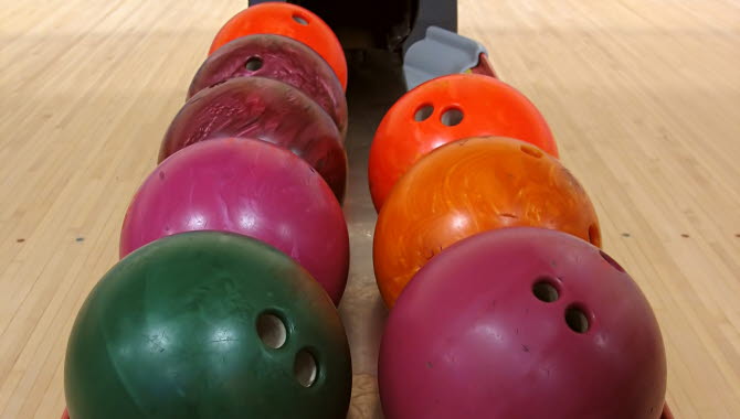 Bowlingklot i olika färger som ligger på en skena. Bowlingbanan syns i bakgrunden.