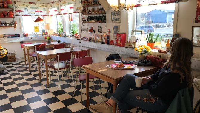 Ett café som är inrett i 50-talsstil med rutigt golv och röda stolar. En kvinna sitter i förgrunden med ryggen mot fotografen