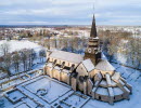 Drönarbild över Varnhems klosterkyrka med snö på taket och det omkringliggande landskapet.