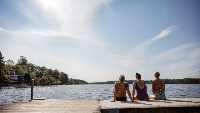 Tre kvinnor sitter på en brygga vid en sjö.