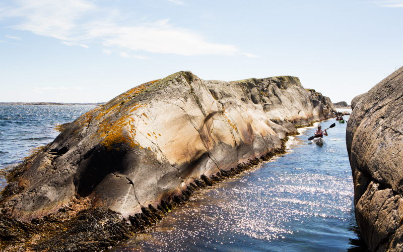 A person in a kayak is paddeling through a narrow canal between two cliffs.
