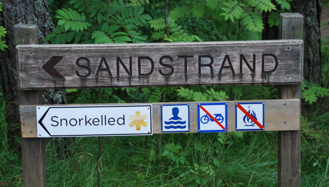 Träskylt som visar vägen till strand med snorkelled på ön Saltö