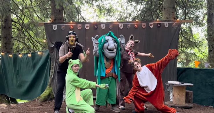 Fem utklädda karaktärer, inklusive en trollmaskot och djurdräkter, poserar glatt framför en utomhusscen i skogen. Alla visar tummen upp eller poserar lekfullt mot kameran.