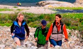 Three people are hiking across a cobblestone field at North Koster. 