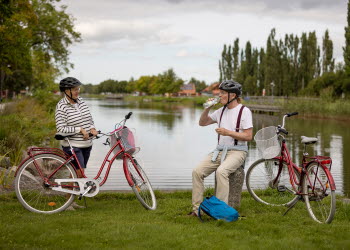 Ett par som vilar i närheten av sina cyklar. I bakgrunden syns ett vattendrag