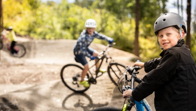 Barn och unga cyklar över grushinder i skogen.
