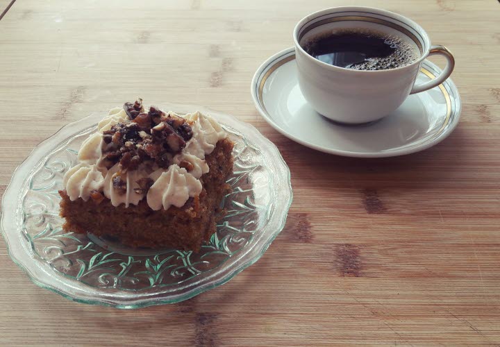 En bild på en kopp kaffe och en kaka på ett fat som står på ett bord.