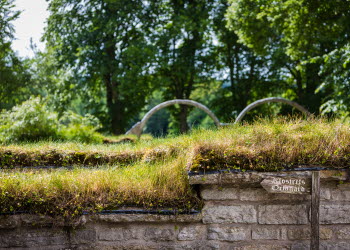 Stone wall under a lawn with trees and two stone arches in the background.